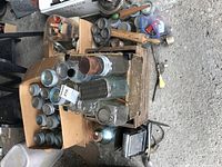 Overview of vintage glass jars, some in cardboard box, along with wooden and metal utensils scattered on ground