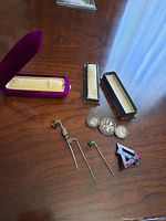Vintage pins and brooches laid out on wooden surface with original boxes for some items.