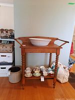 Wood washstand with turned legs, rectangular top with side rails, with a white ceramic bowl on top, a lower shelf with cups not included in sale.