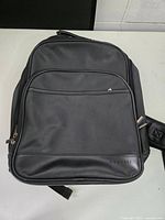 Front view of black Bugatti backpack with zippered front pocket and embossed logo on bottom right corner