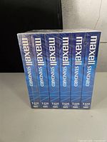 Front view of six sealed Maxell Standard VHS videocassettes in original packaging, stacked vertically showing the Maxell label and T-120 format.