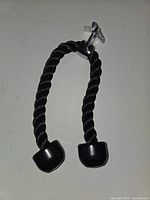Black tricep rope attachment with metal clip, photographed hanging on wall