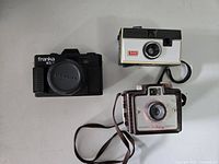 Front view of three vintage film cameras: Franka MX-I, Kodak Instamatic 134, Brownie Holiday 127, showing design and condition.