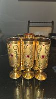 Front view showing six gold-tone goblets with red decorative gems and scroll design.