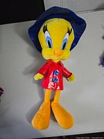 Front view of large vintage Tweety Bird plush wearing blue rain hat and red raincoat, standing on a white surface.
