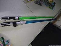 Two vintage Star Wars light sabers with green and blue blades displayed on a white table surface.