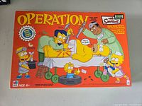Front of vintage The Simpsons Operation board game box showing Simpsons characters performing surgery on Homer Simpson.