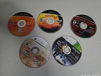 Five Xbox 360 loose discs: Call of Duty Modern Warfare 2, Battlefield 3, Grand Theft Auto IV, and two street racing games.