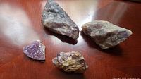 All 4 amethyst specimens of varying sizes placed on a wooden surface showing crystal formations and rough mineral texture.