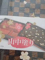 Boxed bento box packaging showing black and red multiple compartments with floral designs on the lid and box.