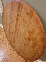 Round butcher block table top standing vertically against wall, showing wood grain and surface wear.