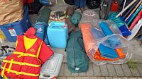 Photo showing red and yellow Sea Nautic life vest, blue plastic cooler, two blue water jugs, rolled tents and sleeping bags packed in bags with brand Hillary visible.