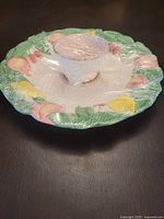 Top angle photo showing round ceramic platter with central bowl, decorated with colorful fruit motifs on the rim and pale pink glazed bowl.