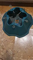 Top view of the green plastic Christmas tree stand showing the star-shaped base, four metal screw bolts with eyelets, and water reservoir.