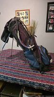 Side view of blue and black Sun Mountain golf carry/stand bag on table showing stand legs and shoulder strap.