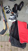 Full set of men's hockey equipment items including skates, shin pads, gloves, sticks, and sports bag displayed on concrete floor.