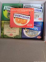 Photo of multiple boxes of assorted HEM Incense Cones in a cardboard box, each labeled with different scents including Mandarin, White, Myrrh, and Patchouli.