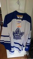 Front view of the Koho Toronto Maple Leafs hockey jersey hanging on a hanger, showing the team logo and tags.