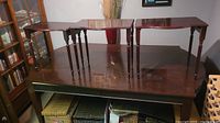 Three dark wooden end tables with spindle legs set side by side on a larger wooden surface.
