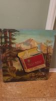 Photo of vintage wooden Pall Mall cigarette advertising sign with scenic outdoor background including deer and mountains.