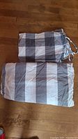 Folded cotton duvet cover and two pillow shams laid on wooden floor. Visible tie closures and reversible pattern colors including gray and white tones.