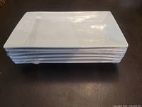 Stack of six white rectangular ceramic dinner plates wrapped in plastic showing size, shape and condition.