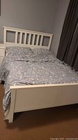 Full view of the assembled white wood full bed with bedding, mattress, and mattress protector in a bedroom setting.