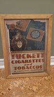 Photo displaying full view of framed vintage Tuckett Cigarettes and Tobaccos advertisement measuring 13x17.5 inches with wood frame and visible print details.