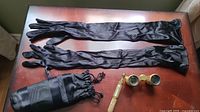 Black satin long evening gloves, a black drawstring pouch, and vintage mother of pearl and brass opera glasses on a wooden surface