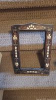 Wooden picture frame showing detailed Mother of Pearl inlay with floral and scroll patterns, resting on carpeted stairs.