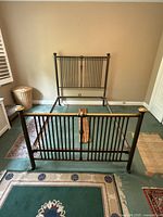 Full view of antique solid brass 4 post bed frame with headboard and footboard showing vertical rod design and wooden cross braces on floor.