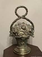 Full view of the brass flower basket door stopper standing upright showing entire body and handle loop.