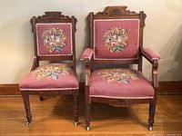 Two antique Eastlake style chairs with needlepoint floral upholstery on pink fabric. One armless and one armchair, both with carved wood and turned legs with casters.