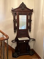 Full view of the antique carved wood hall tree showing mirror, marble stand, drawer, and cast iron umbrella holders.