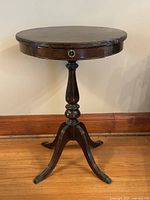 Frontal view of the antique round pedestal end table showing turned pedestal and claw feet.