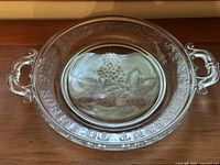Top view of the glass bread plate on wooden surface showing grape cluster and leaves design with embossed inscription around the rim.