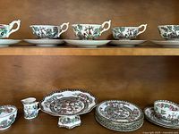 Shelf top row showing six teacups and saucers with floral Indian Tree pattern, gold and brown trim, scalloped rims.