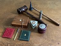 Photo of assorted antique items on wooden table including wooden gavel, candle snuffer, wooden boxes, pill box, letter opener, and small bound books.
