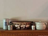 Wide shot of all pottery items on wooden surface showing oval dish, stein, jam pot, miniature bottle, and crock