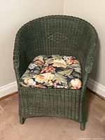 Full frontal view of the dark green wicker chair with floral cushion, showing the curved backrest and woven texture.