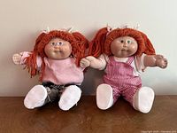 Front view of the pair of two Cabbage Patch Kids dolls sitting side by side on a wooden surface, showing detailed faces and outfits.