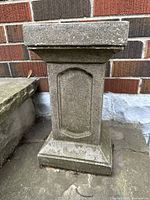 Front view of the vintage cement garden pedestal showing the rectangular shape, recessed panels, and weathered texture.