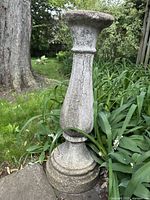 Full view of the vintage cement garden pedestal showing its height, shape, and weathered texture in an outdoor garden setting.