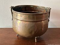 Side angle view showing the copper planter with handle and three feet, highlighting the patina and slight dents on the surface.