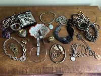 Full view of the collection of costume jewelry spread out on a wooden surface including necklaces, bracelets, rings, earrings and wristwatch.