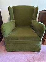 Front view of green velvet wingback chair showing seat, backrest and armrests.