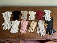 Full collection of 12 pairs of women's vintage gloves displayed on wood surface, showing variety of colors and styles.