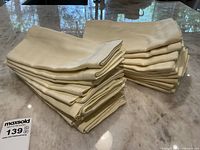 Two neatly stacked piles of folded pale yellow cotton napkins on a glass table, showing color and fabric texture.