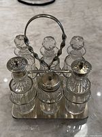 Front view of the antique silver plated condiment caddy with six crystal bottles and faceted stoppers, two shaker bottles visible and the central lidded container.
