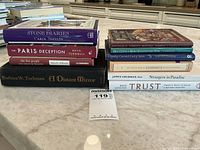 Photo showing stacked books including Stone Diaries, The Paris Deception, The Five People You Meet in Heaven, A Distant Mirror, and others on a kitchen counter.